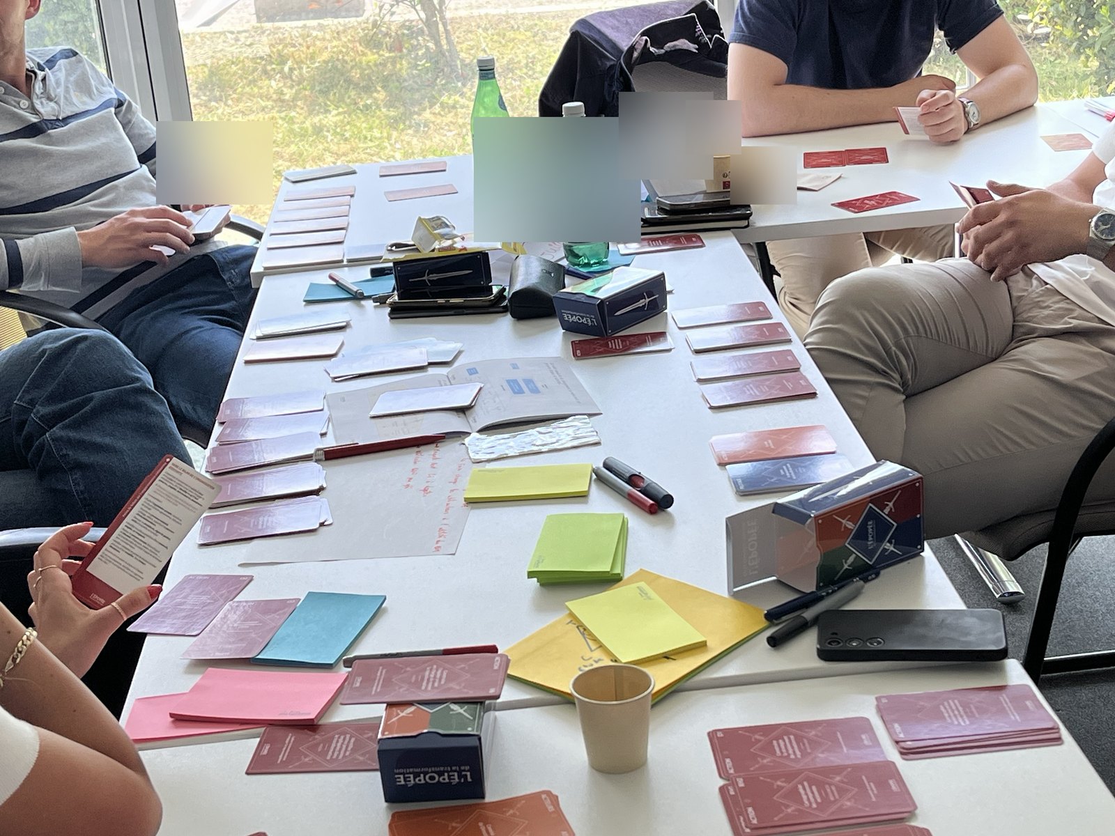 Une équipe installée autour de la table, les cartes de l'Épopée disposées et les boîtes de jeu ouvertes